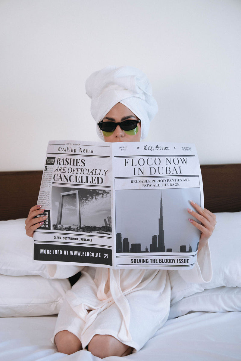 Person holding a newspaper with text about FLOCO reusable period panties in Dubai.